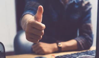 person sat at a desk with one hand raised in a thumbs up gesture