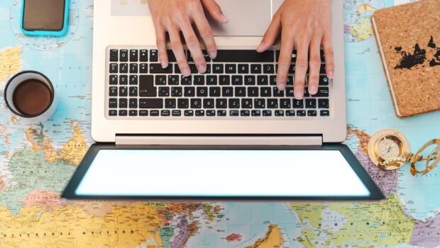 image of two hands typing on a laptop on a desk covered in a map of the world