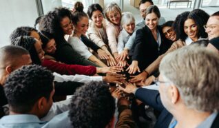 Large group of people stood in a circle in an office building with their hands all together