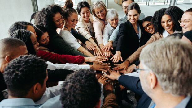 Large group of people stood in a circle in an office building with their hands all together