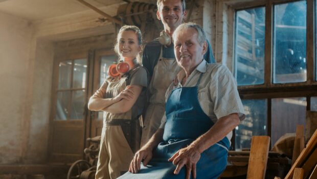 photo of 3 people of varying ages stood next to each other in aprons and hearing aids with a workshop in the background