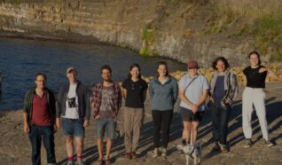 Photo of 8 people stood in a line at the top of a cliff smiling