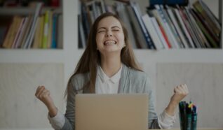 photo of a woman sat at a desk in front of a laptop celebrating