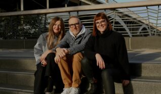 3 people sat on a step outside smiling at the camera