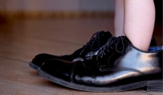 child stood in mans black dress shoes