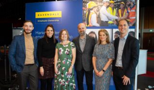 Photo of Alex, Simon, Ewan, Lindsay, Hannah and Emily on front of their promotional stand at the employee ownership association conference